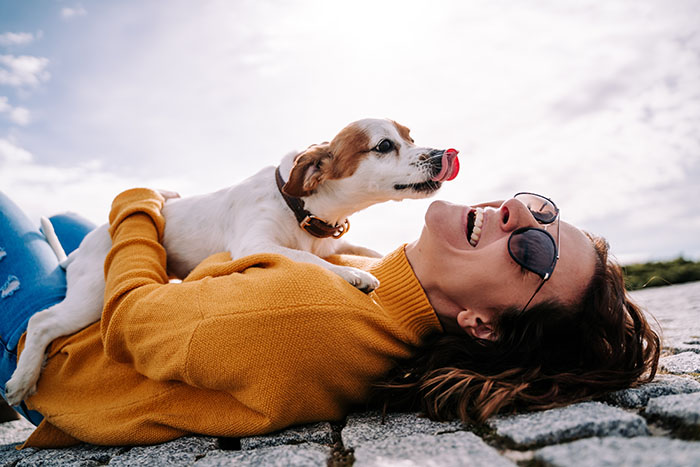 Girl laying on her back with a dog on top of her licking her face.